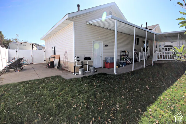 Rear exterior with a covered patio, additional covered area, white vinyl fencing, and concrete patio space with plenty of room for an RV