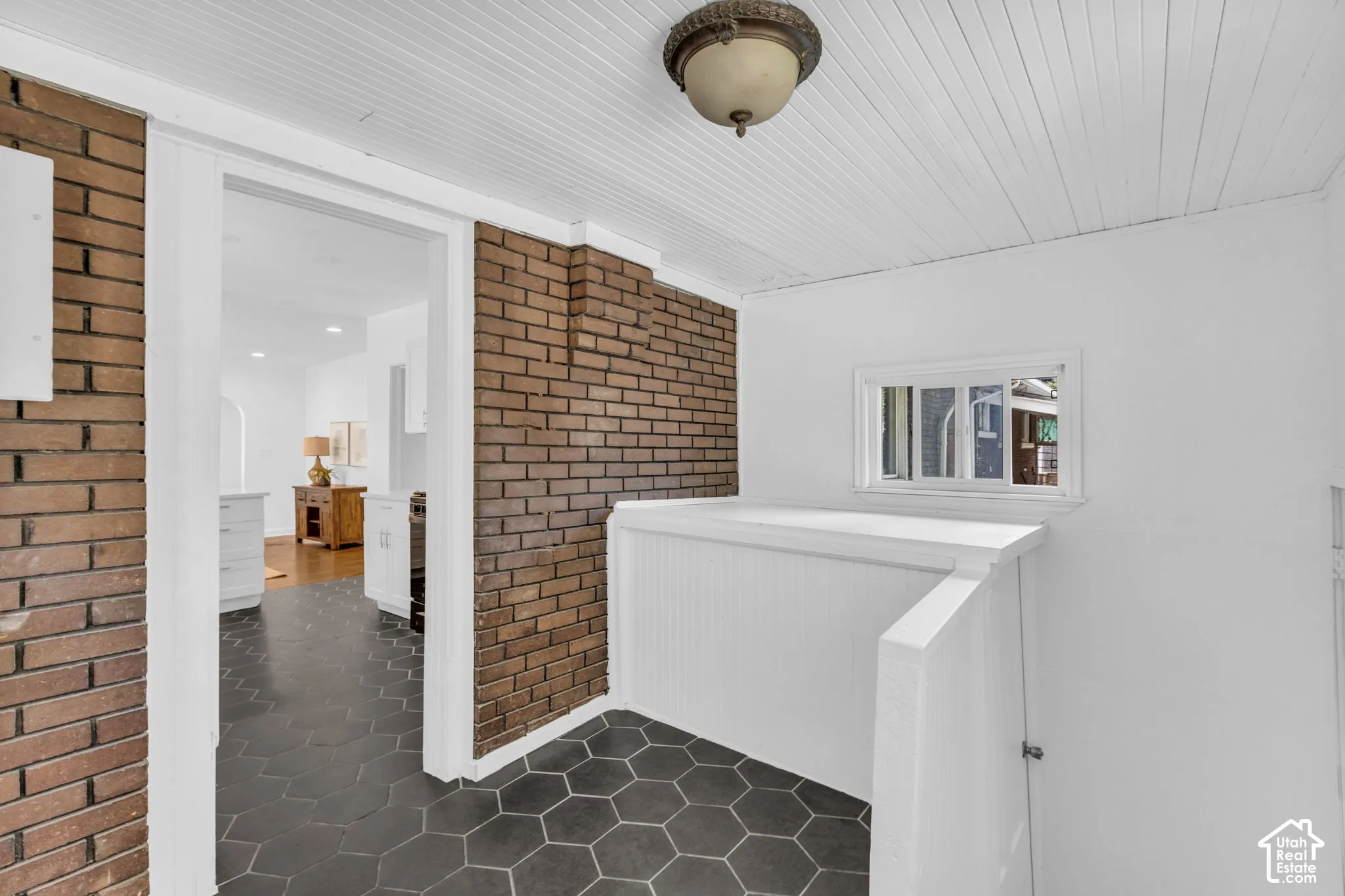 Hexagonal floor tiling, brick wall accents, white shiplap ceiling, white window trim, and white wainscoting
