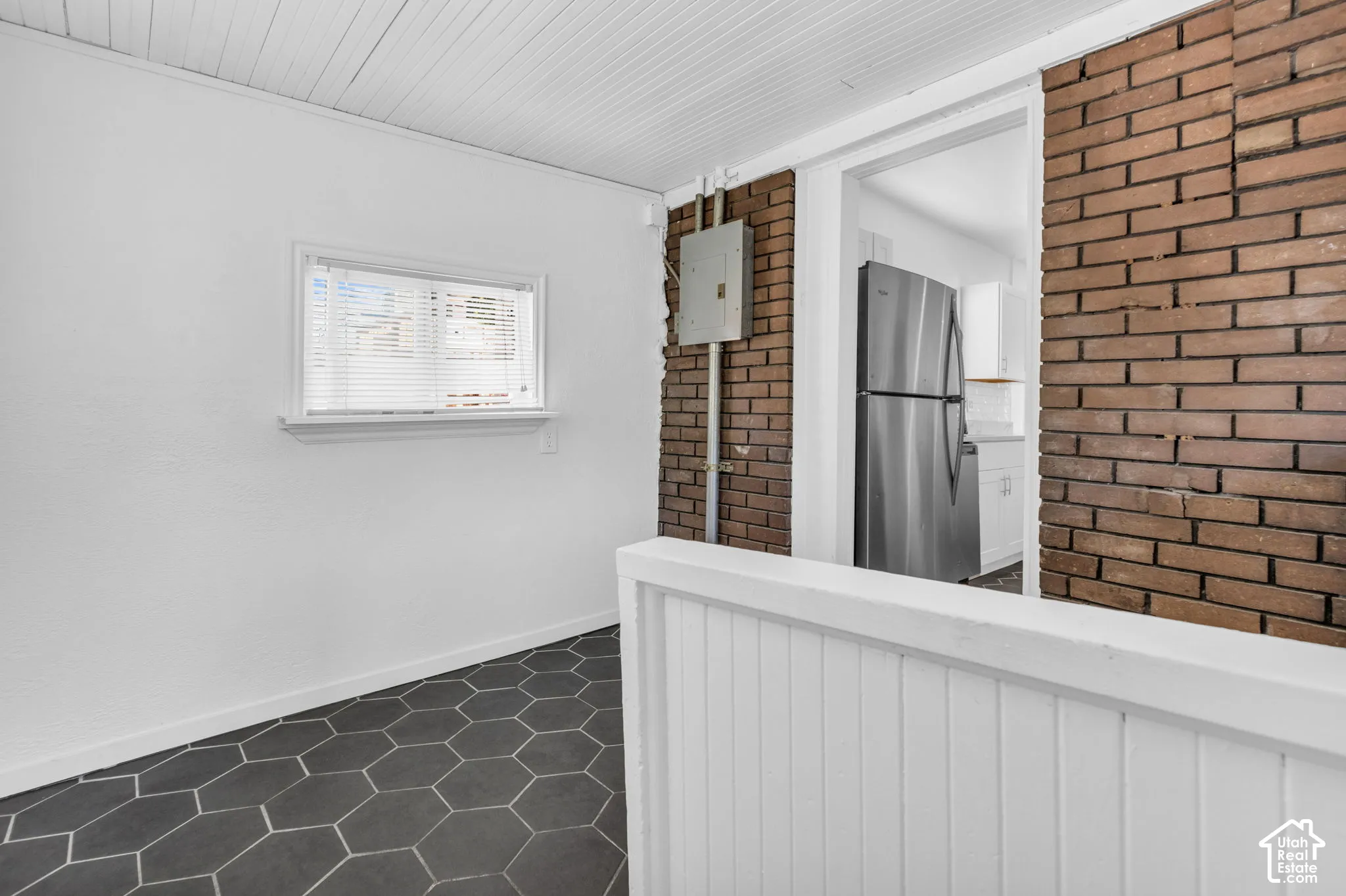 Hexagonal floor tiling, white walls, exposed brick accent wall, white slatted ceiling, and a window with white trim