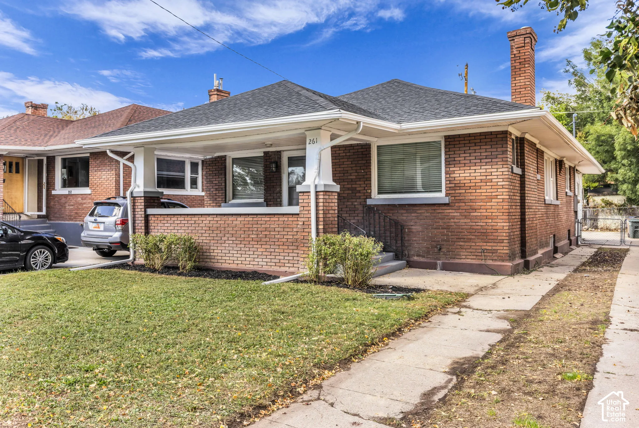 Brick exterior, peaked roofline, front porch with columns, concrete walkway, and a driveway