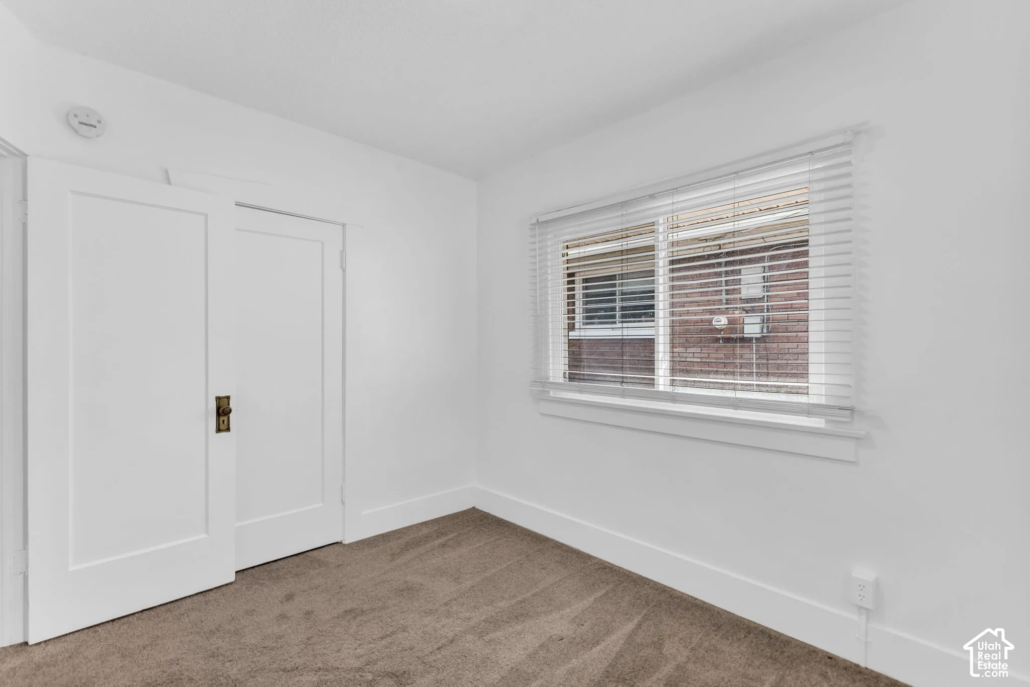 Neutral-toned carpeting, white walls, and a window with blinds