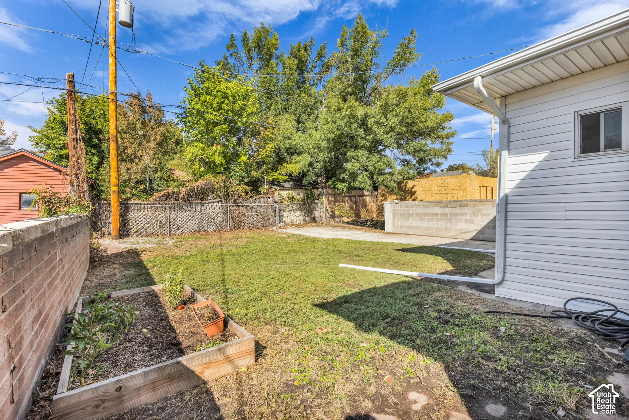 Expansive backyard featuring a manicured lawn, concrete patio, a raised garden bed, and a durable block wall perimeter