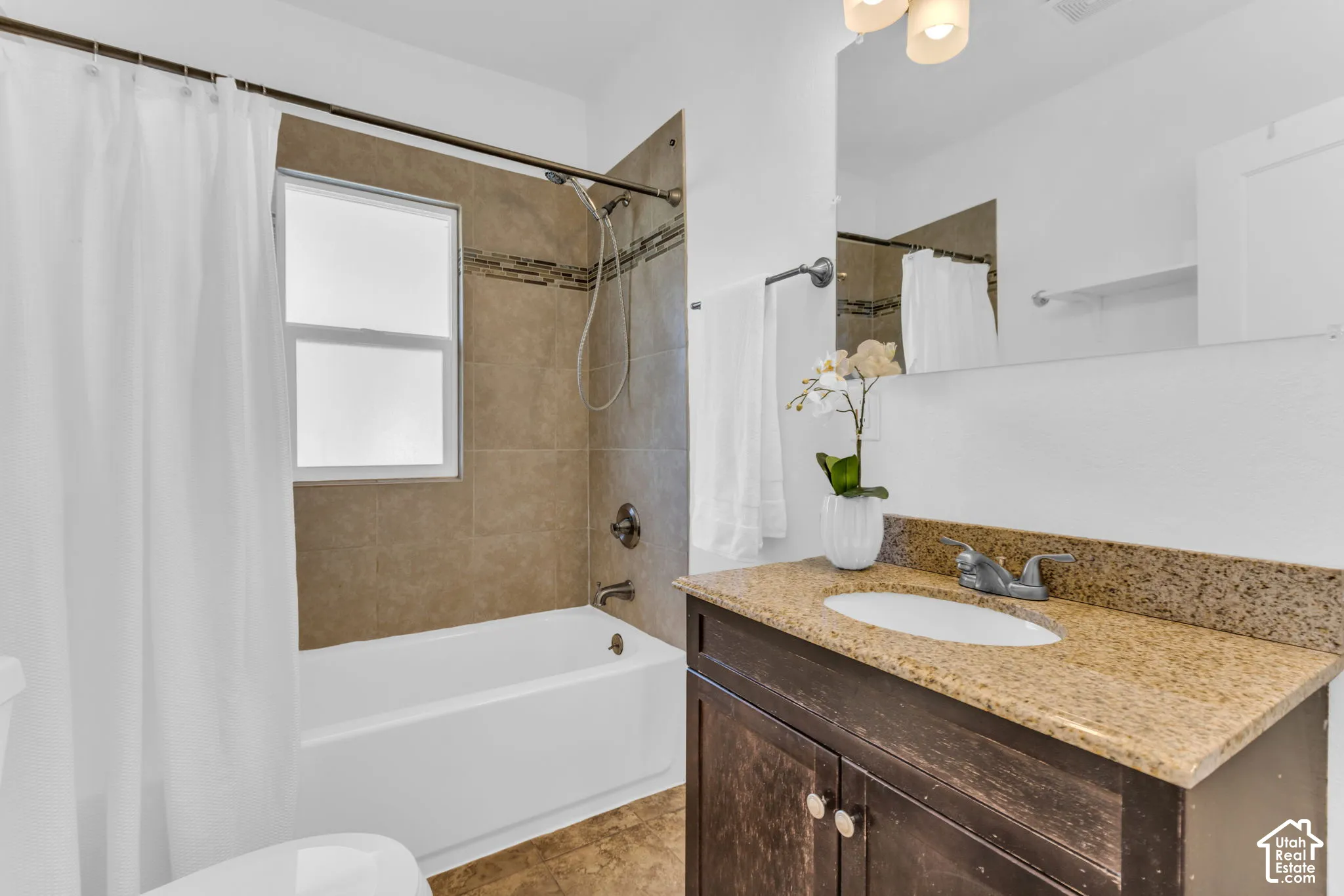 Bathroom featuring a shower/tub combination with tiled surround, a single window, and a vanity with a countertop and undermount sink