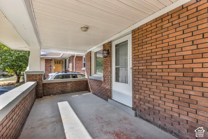 Covered front porch with brick half-walls, concrete flooring, and a white screen door