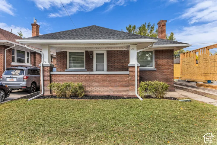 Brick exterior, covered front porch with white columns, dark shingle roof, mature landscaping, and an asphalt driveway