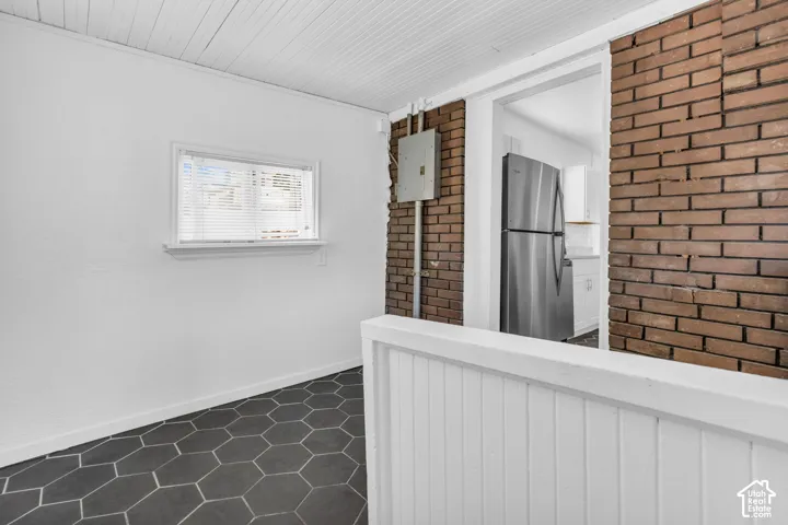 Hexagonal floor tiling, white walls, exposed brick accent wall, white slatted ceiling, and a window with white trim