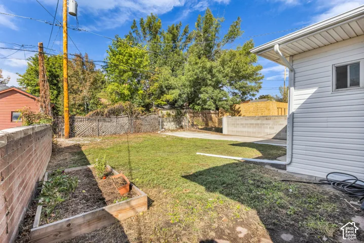 Expansive backyard featuring a manicured lawn, concrete patio, a raised garden bed, and a durable block wall perimeter
