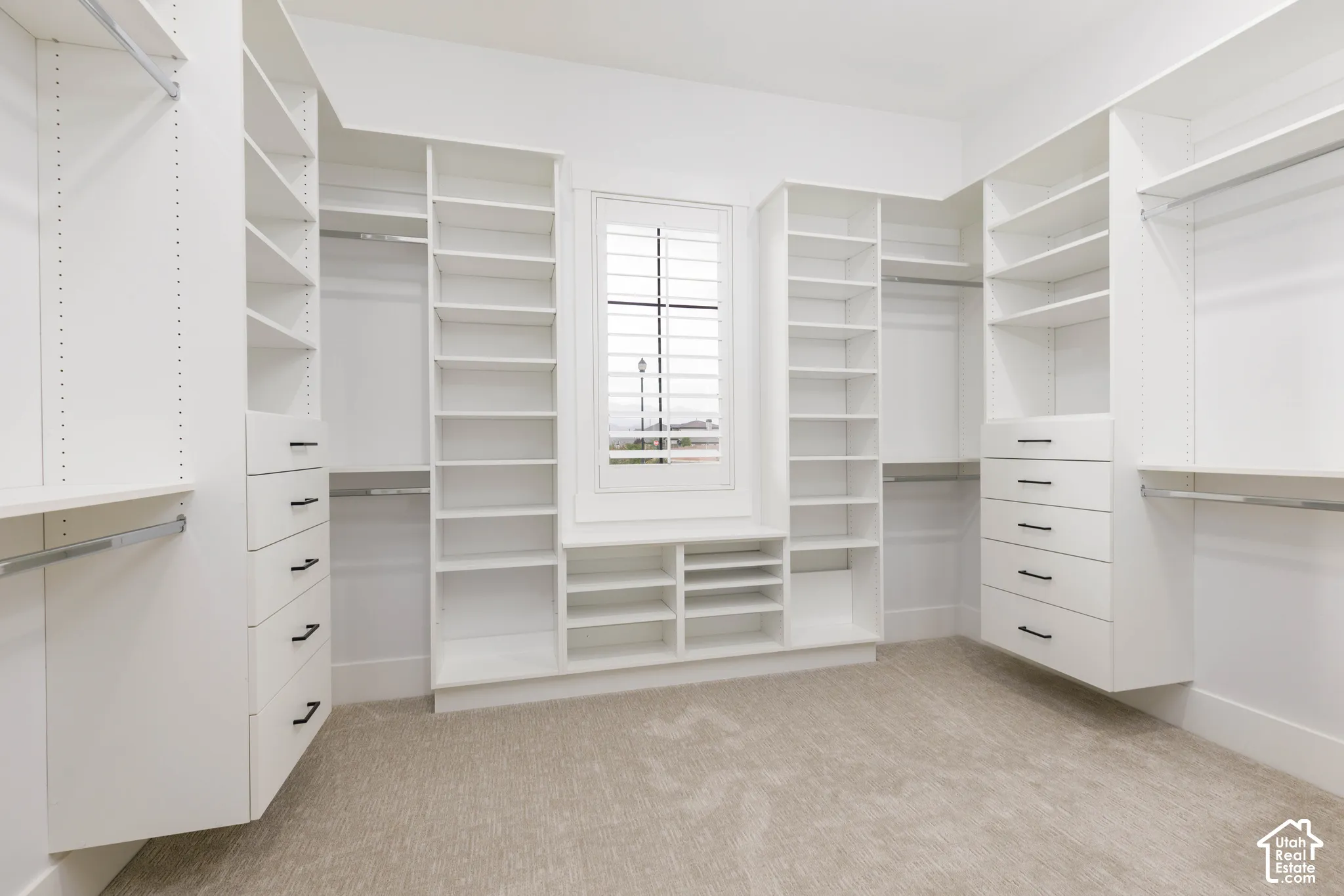 Built-in custom closet system with extensive shelving, multiple hanging rods, integrated drawers with dark hardware, and a window with plantation shutters