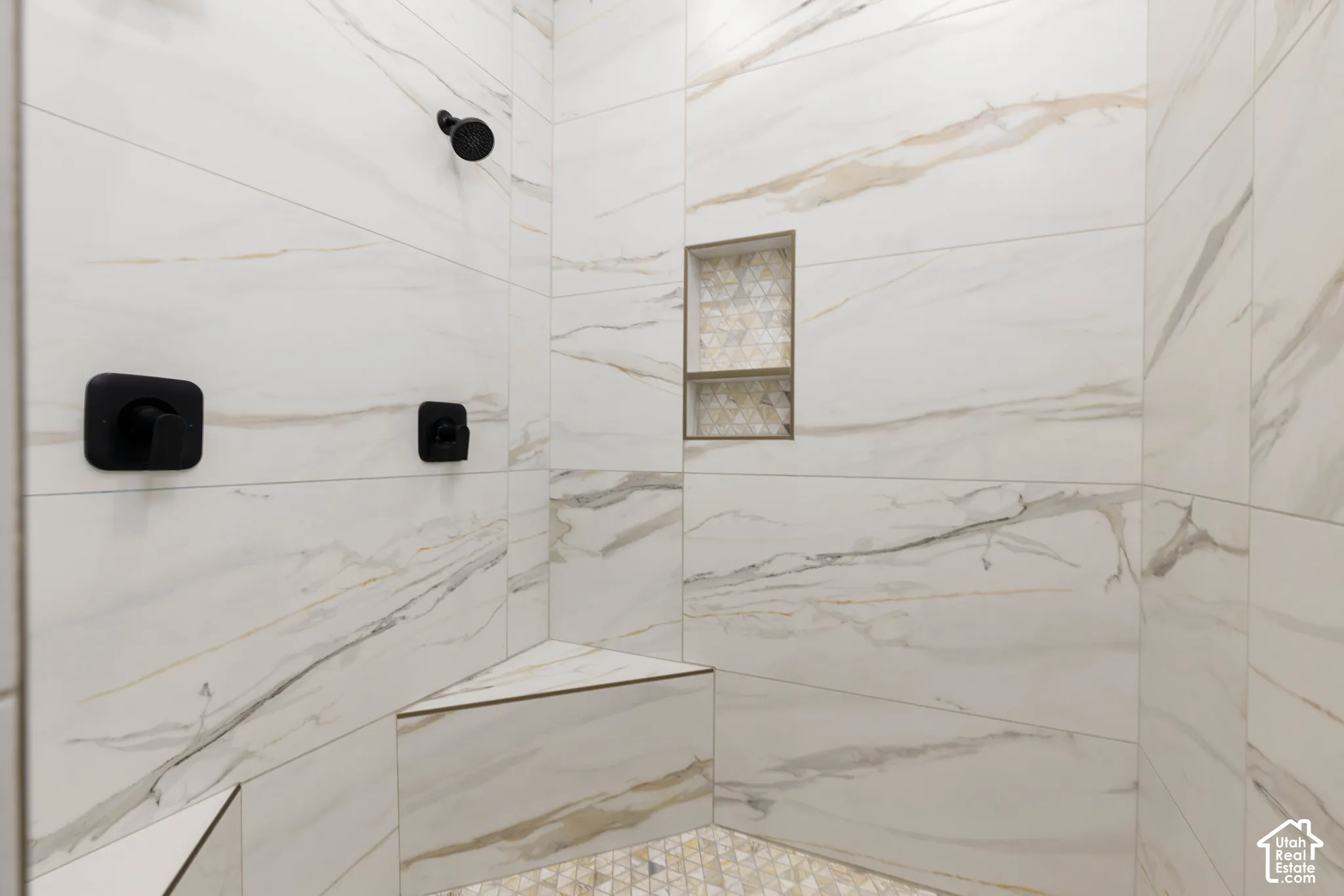 Tiled shower with a built-in bench, recessed niche with decorative tile, and matte black fixtures
