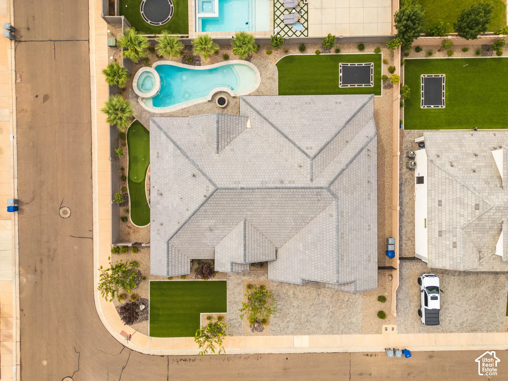 Curved swimming pool with an integrated spa, putting green, lush landscaping, and a tile roof
