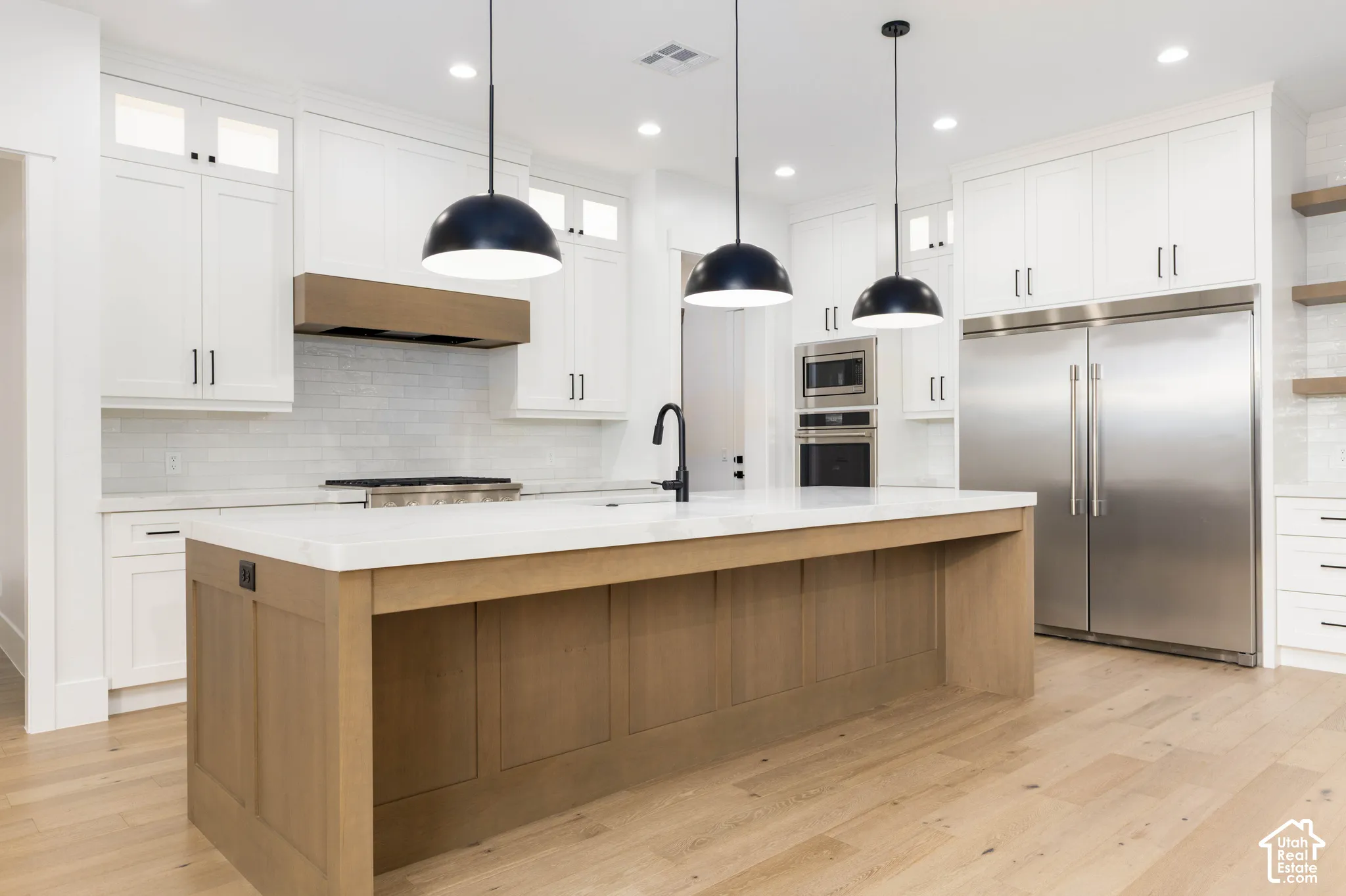 Kitchen featuring a central island, stainless steel appliances, light wood-finish flooring, white cabinetry, and pendant lighting
