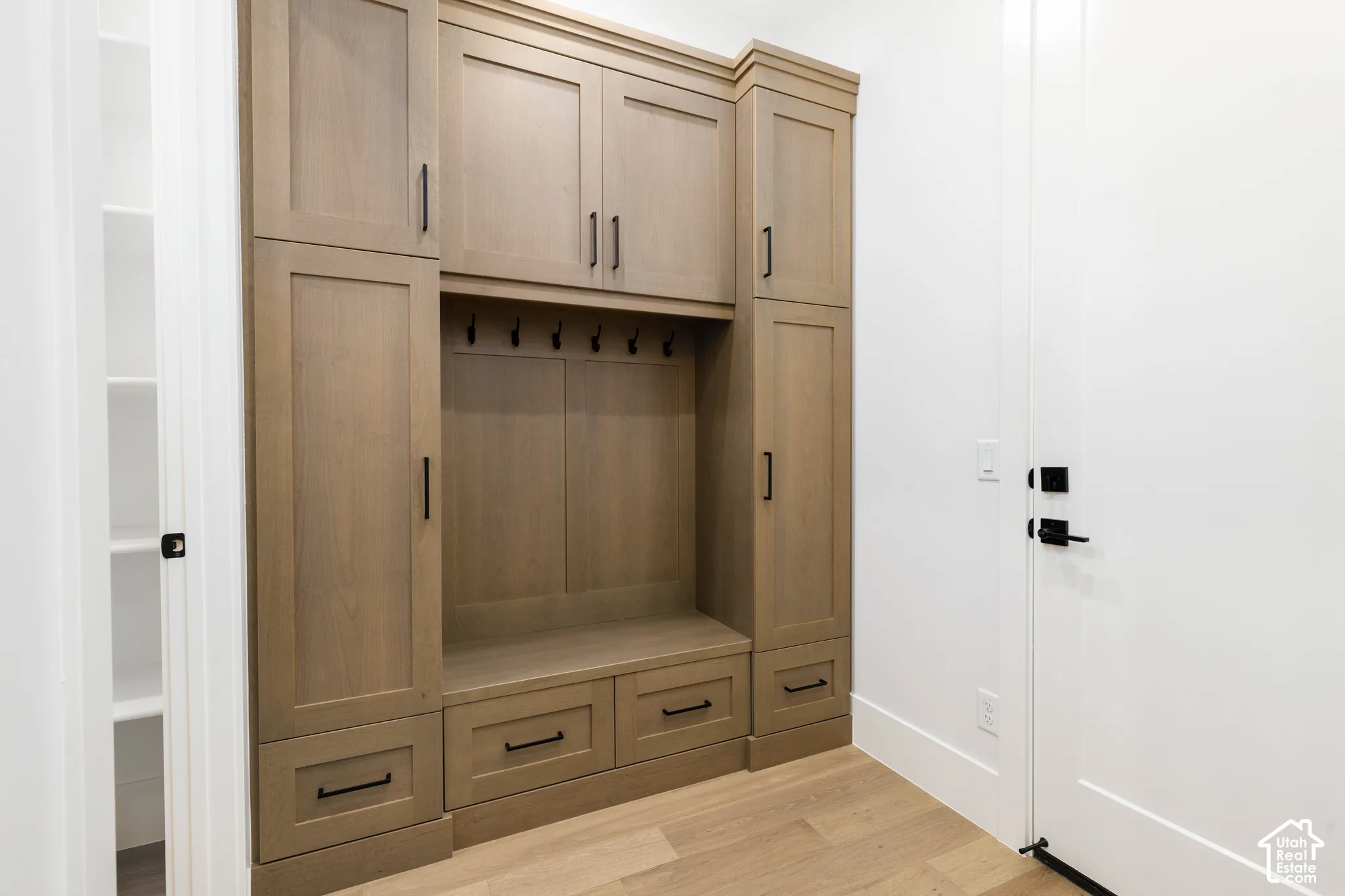 Built-in wood-finish cabinetry with matte black hardware, integrated bench seating, and wall hooks