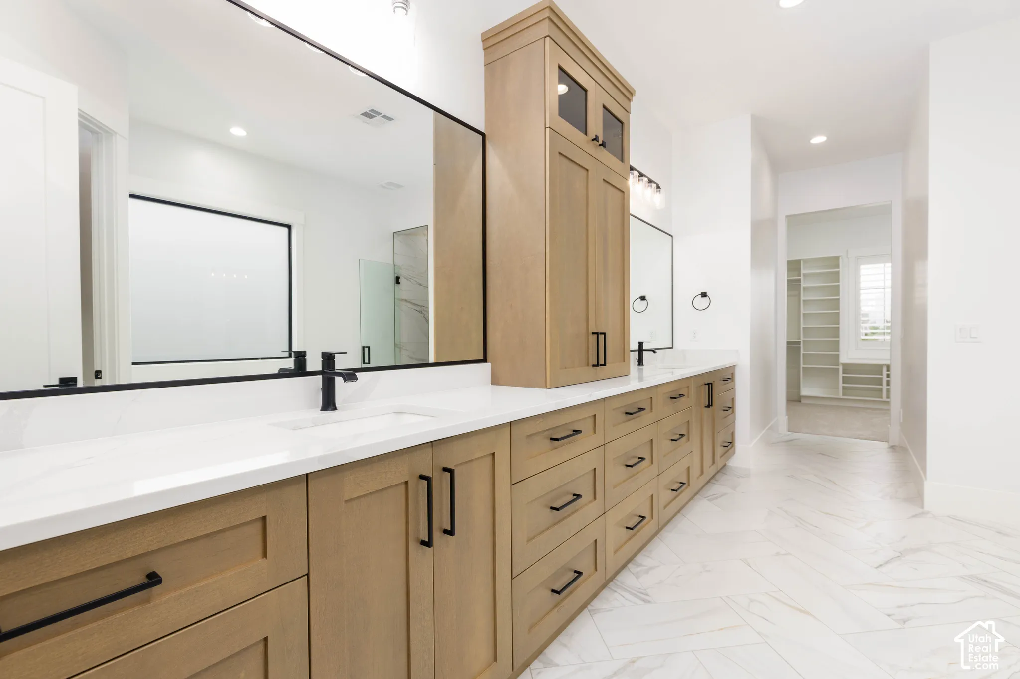 Dual vanity with light wood-finish cabinetry, white countertops, and black fixtures