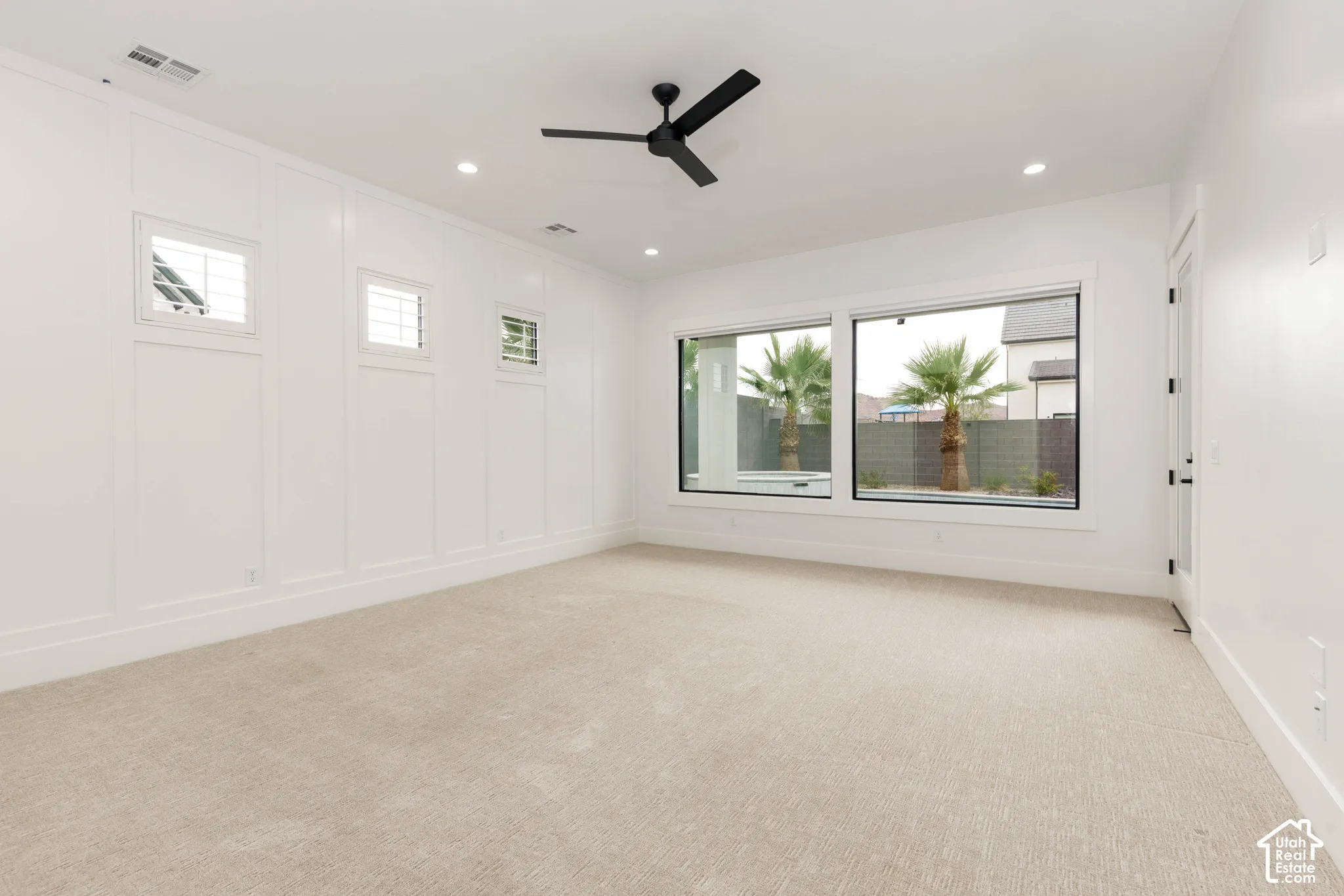 Recessed lighting, large windows, white paneling, ceiling fan, and light-toned carpeting