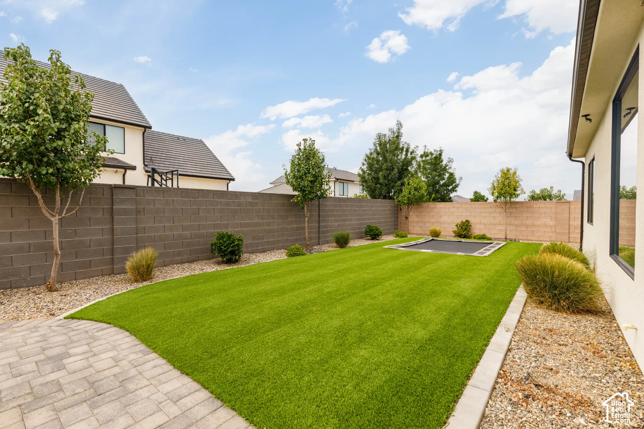 Expansive backyard featuring a lush artificial turf lawn, paver patio, block privacy fencing, and mature landscaping