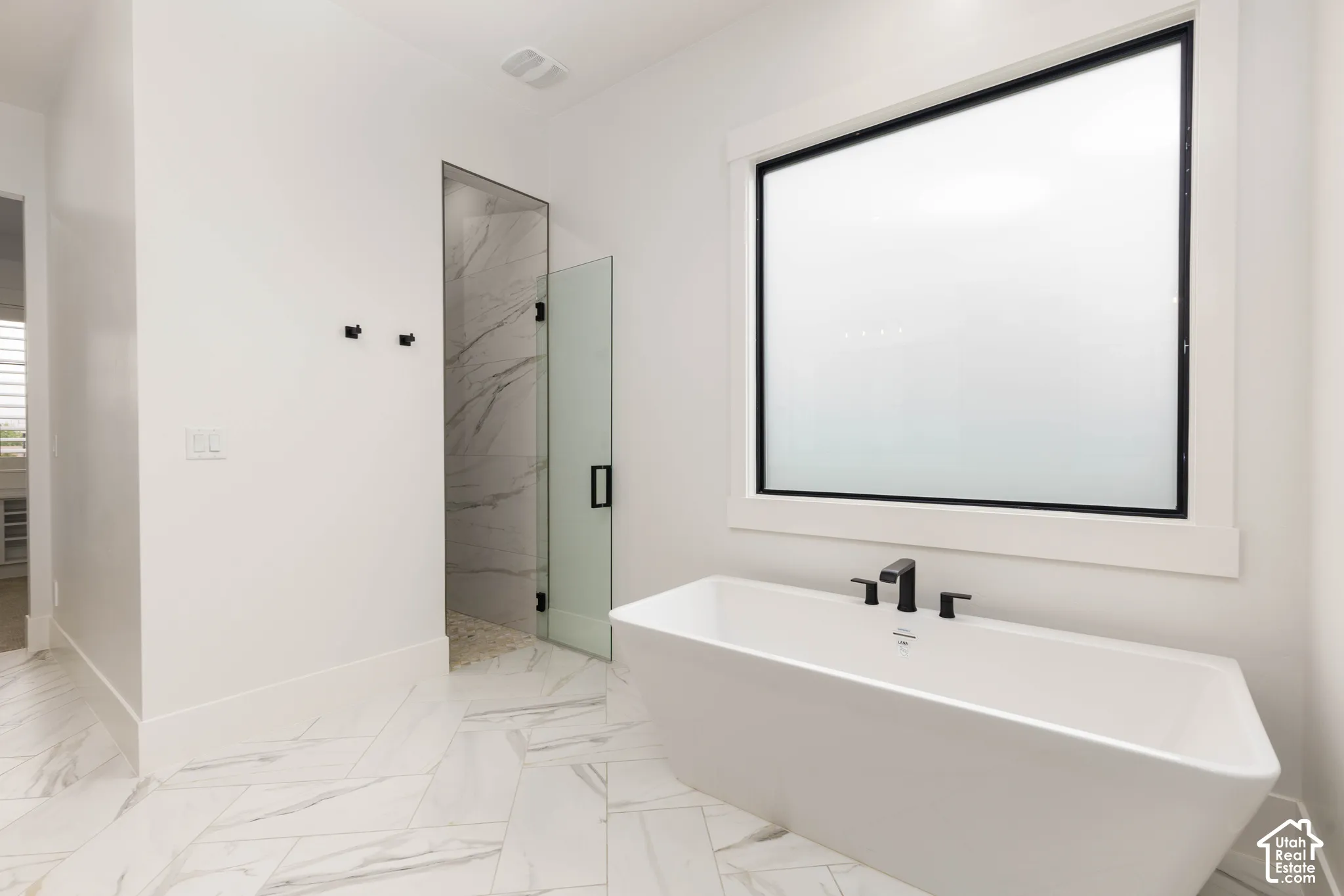 Freestanding soaking tub with matte black fixtures, large frosted window, walk-in shower with glass enclosure, white marble-look shower walls, and patterned tile flooring