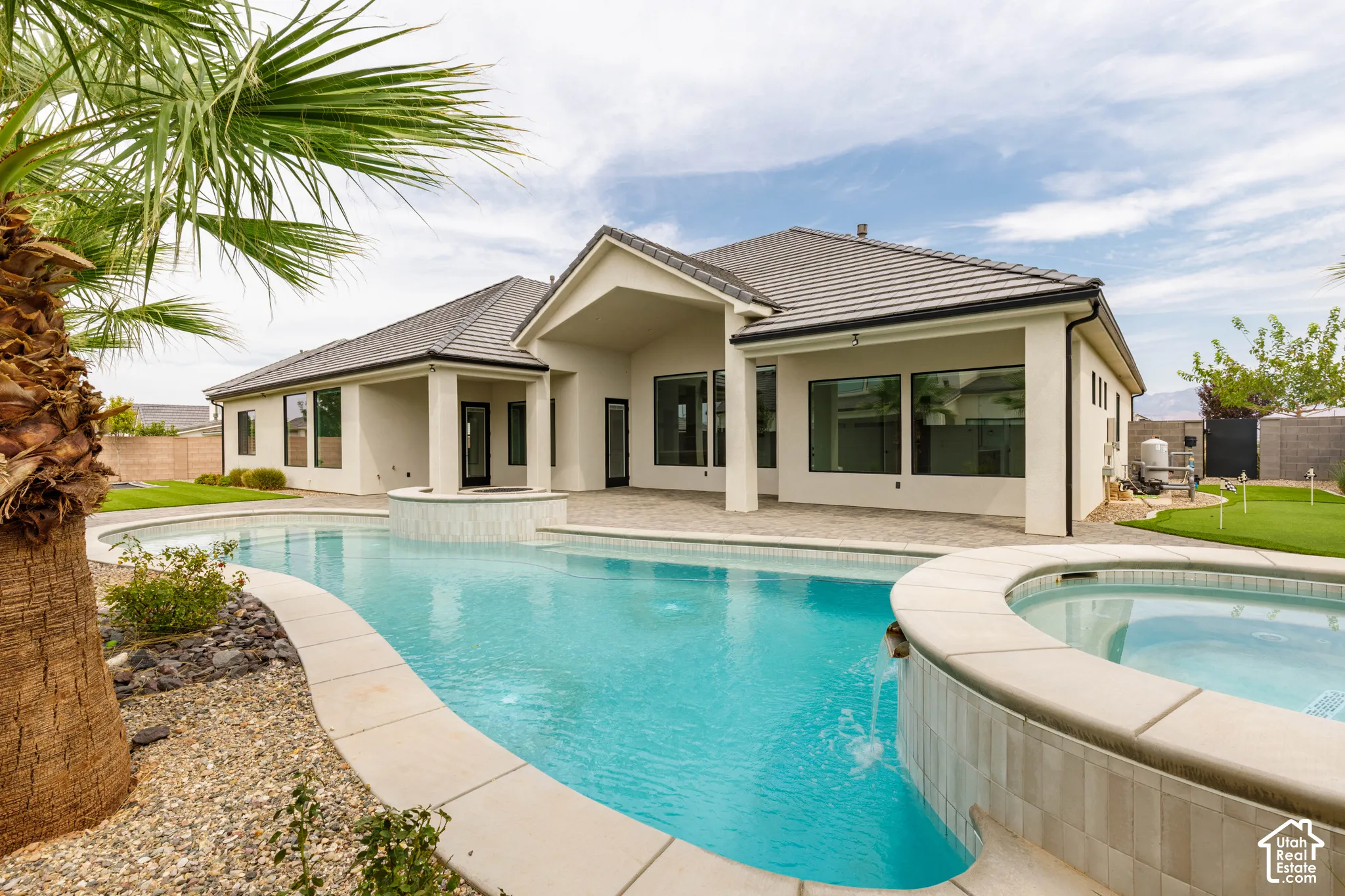 Rear exterior with a curved swimming pool, integrated spa, covered patio, and artificial turf putting green