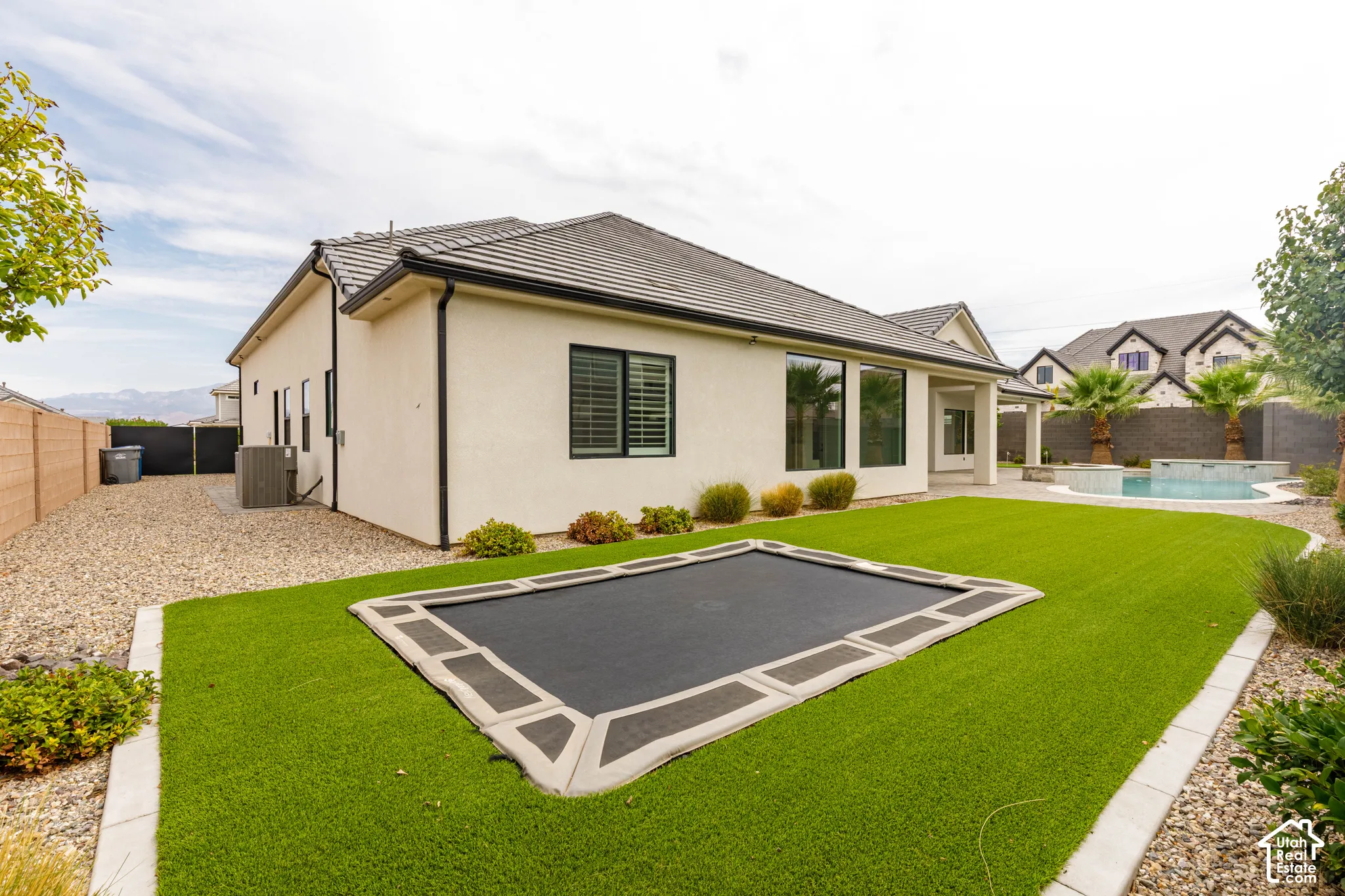 Landscaped backyard featuring artificial turf, a built-in trampoline, and a swimming pool with a spa