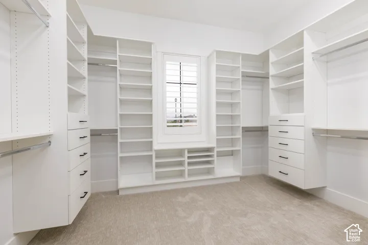 Built-in custom closet system with extensive shelving, multiple hanging rods, integrated drawers with dark hardware, and a window with plantation shutters