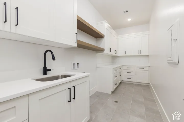 White shaker cabinetry with matte black hardware, stainless steel undermount sink, matte black faucet, light wood-finish floating shelves, and light gray tile flooring