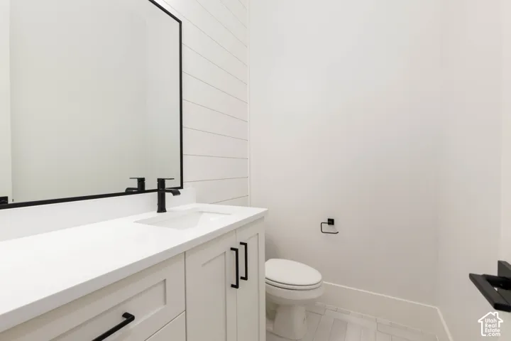 White vanity with integrated sink, black fixtures, black-framed mirror, horizontal plank wall accent, and white tile flooring