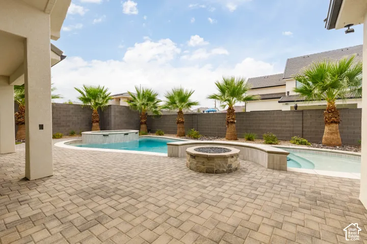 Paver patio with a swimming pool, integrated spa, and a stone fire pit