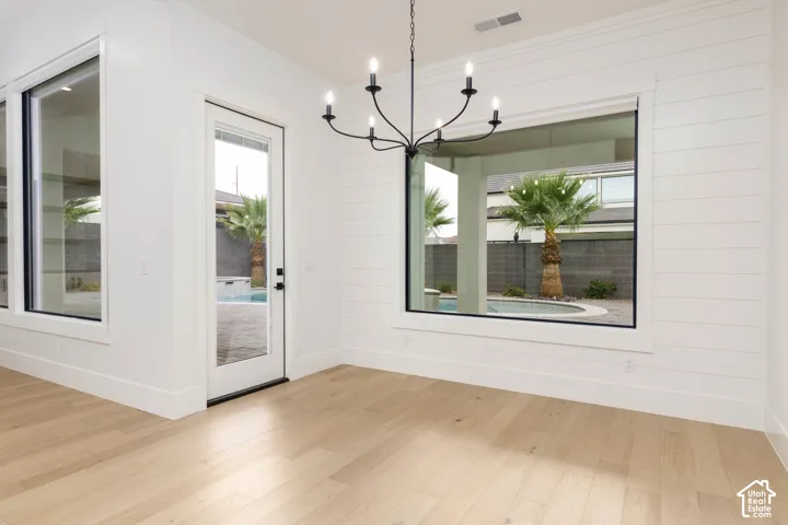 Light wood-finish flooring, white shiplap accent wall, multiple large windows, glass-paneled door, and a black metal chandelier
