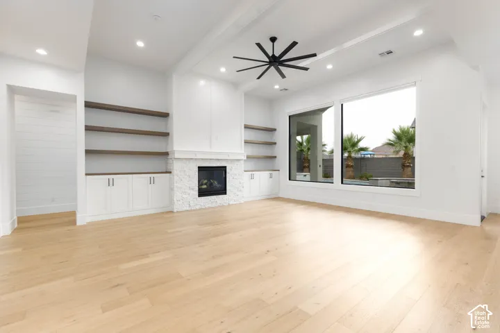 Spacious room featuring light wood-finish flooring, a stone-clad fireplace, integrated shelving with lower cabinetry, and large picture windows