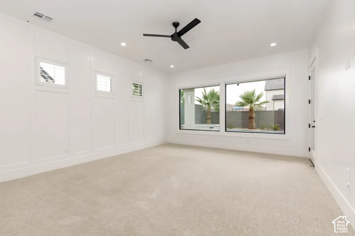 Recessed lighting, large windows, white paneling, ceiling fan, and light-toned carpeting