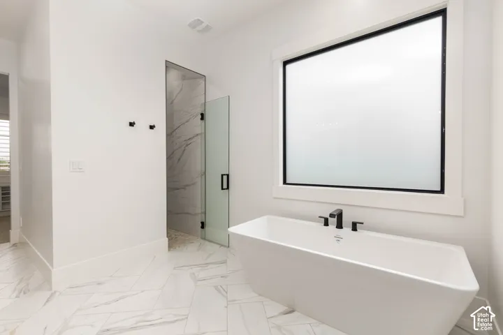 Freestanding soaking tub with matte black fixtures, large frosted window, walk-in shower with glass enclosure, white marble-look shower walls, and patterned tile flooring