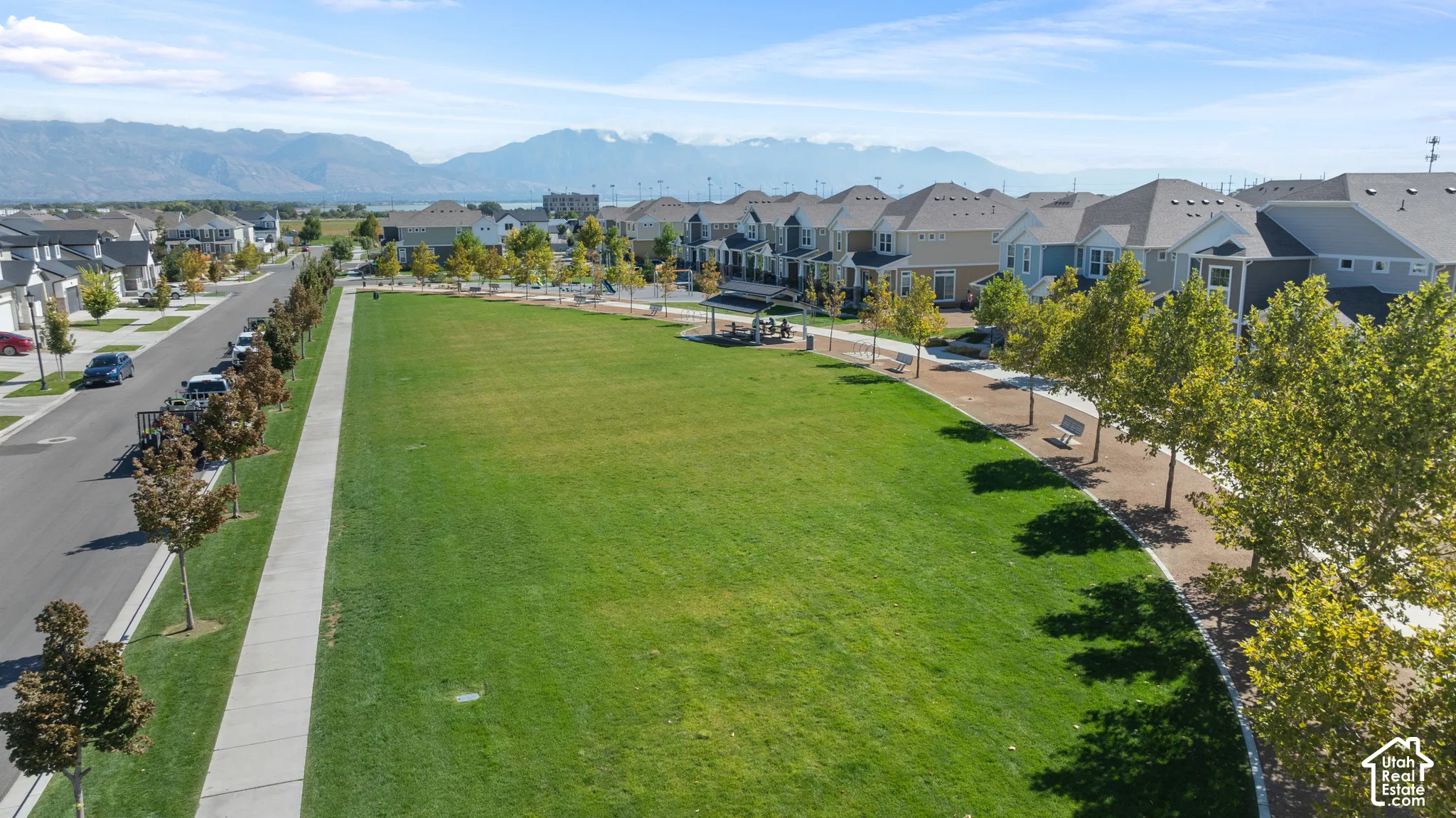 Expansive green space featuring a paved walking path, mature trees, and mountain backdrop