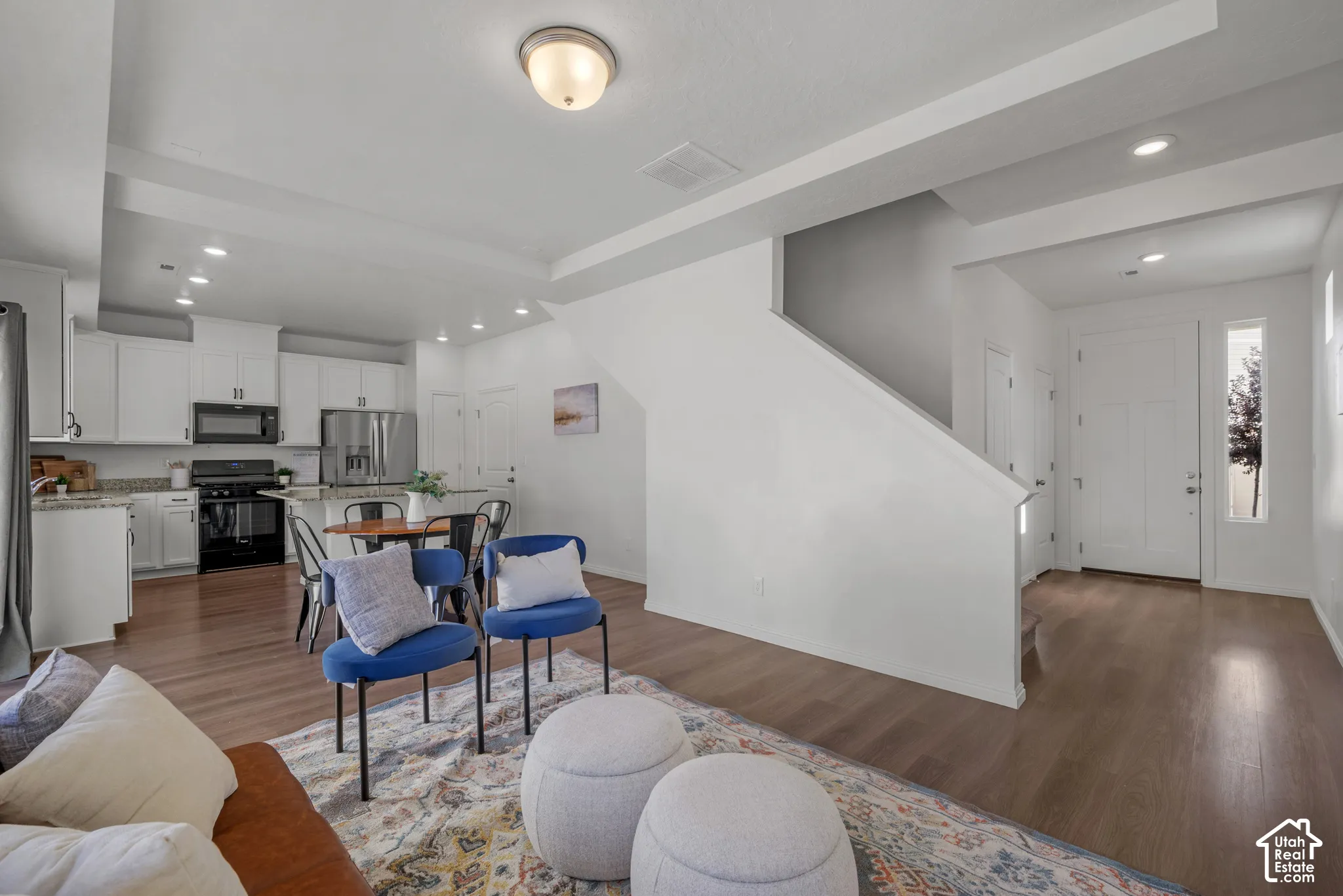 Open-concept living area with wood-finish flooring, recessed lighting, and a modern kitchen featuring white cabinetry and stainless-steel appliances