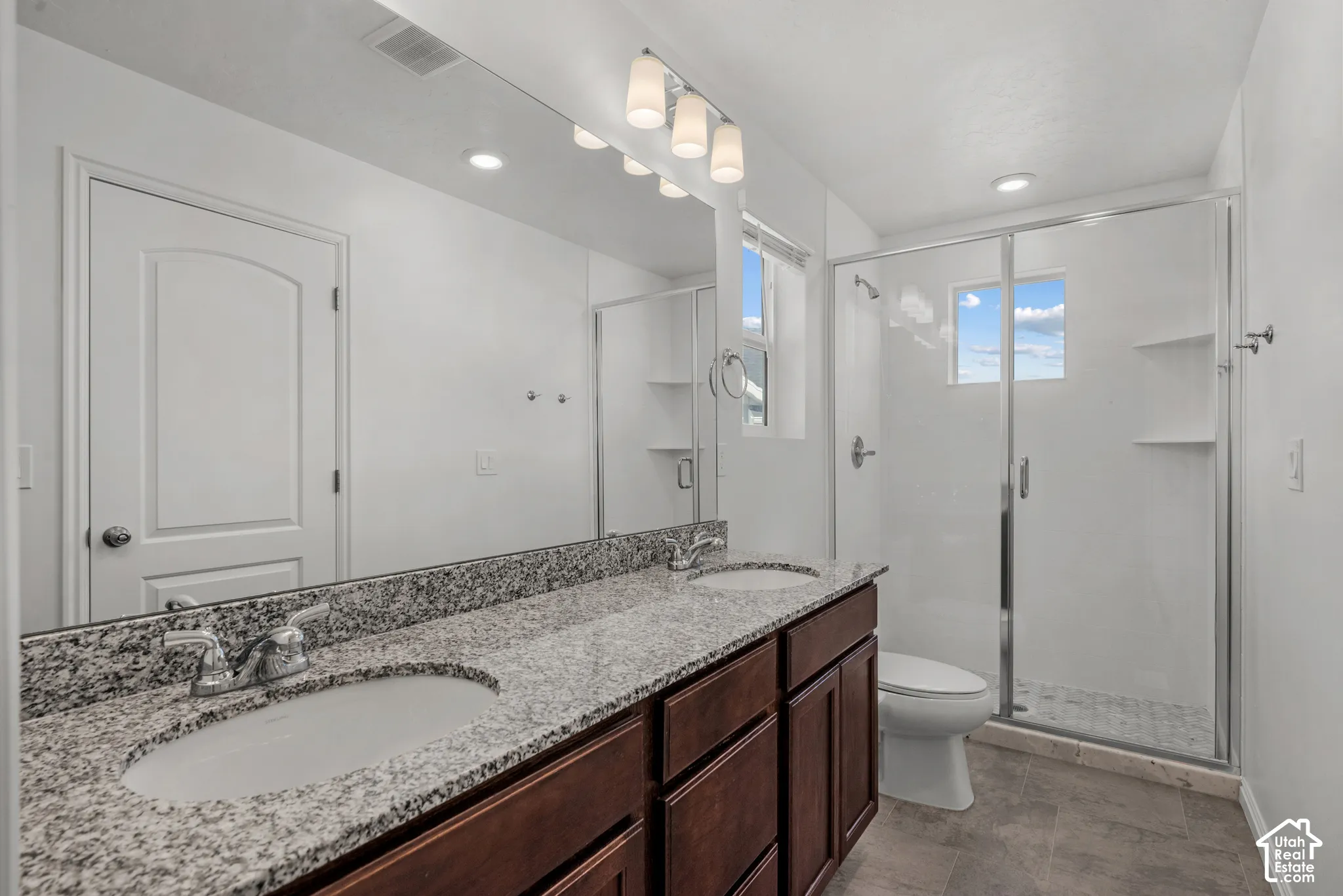 Dual vanity with stone-finish countertop, wood-finish cabinetry, and  dule undermount sinks, walk in shower, glass shower door