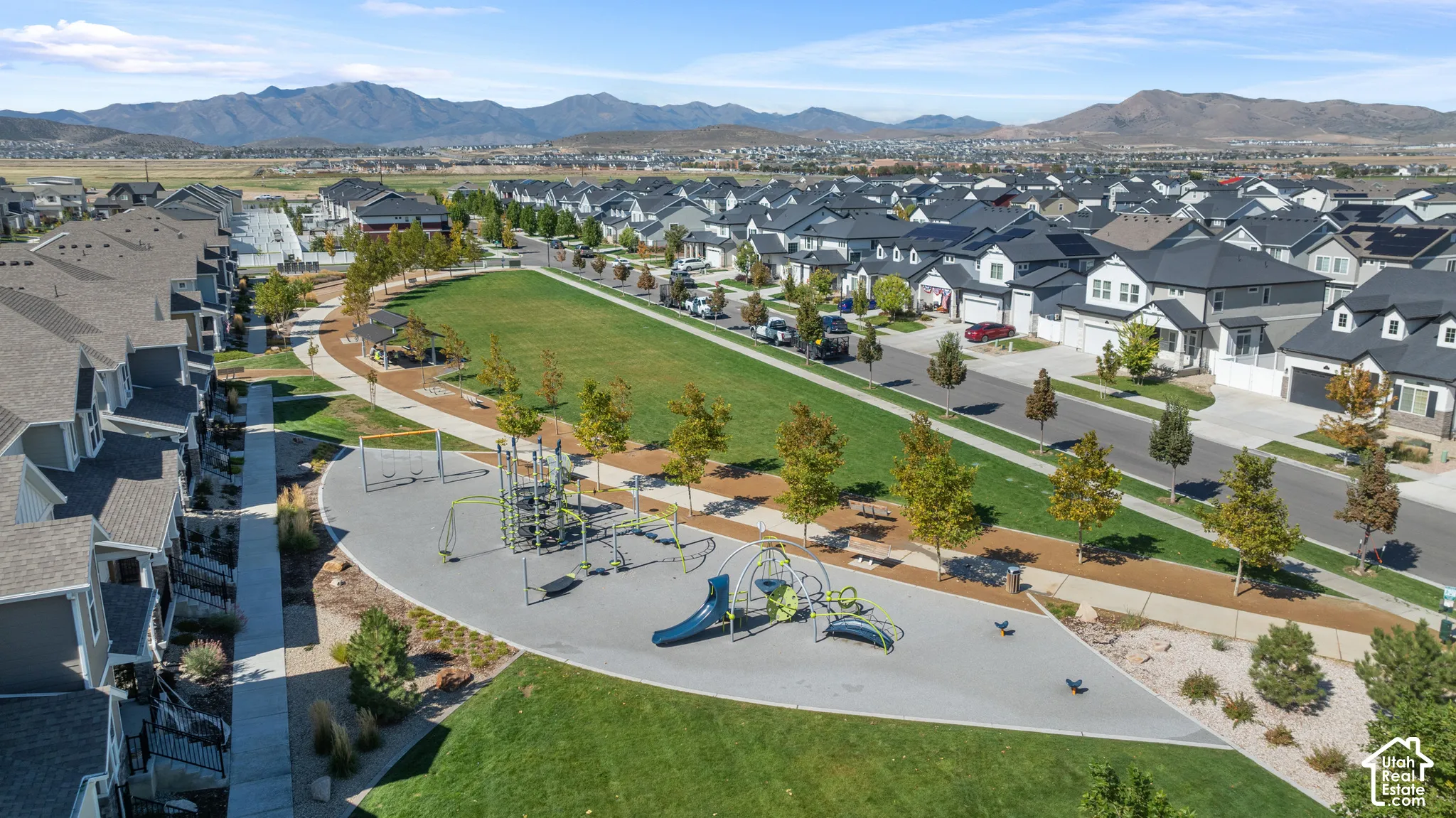 Expansive green space featuring a playground, walking paths, mature trees, and covered picnic area