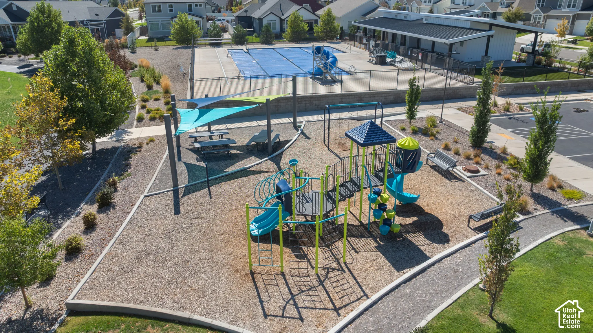 Community playground with multiple play structures, adjacent to a pool area and green space, featuring shade canopies and picnic tables