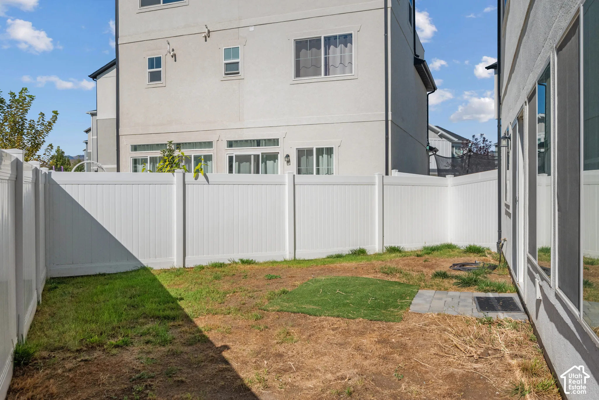 Enclosed backyard featuring white privacy fencing, a ground-level patio, and sliding glass doors