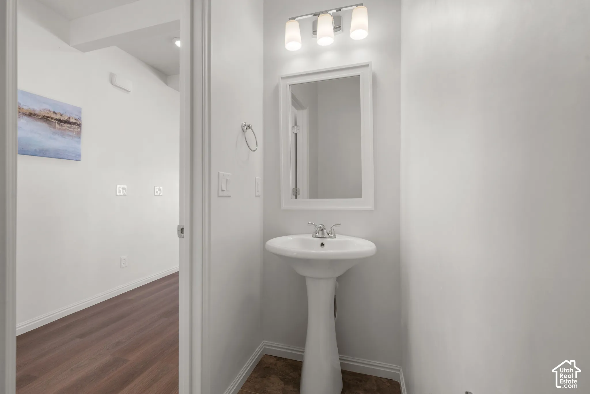Pedestal sink with chrome faucet, framed mirror, and a three-light vanity fixture. Main level half bath