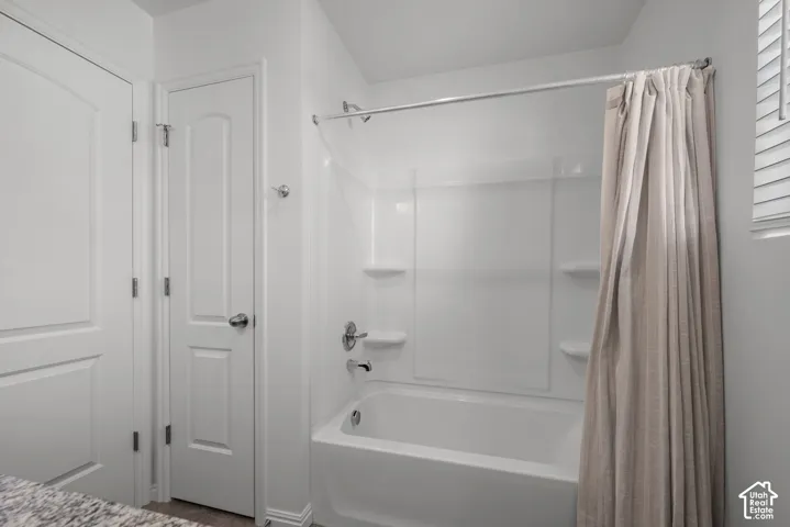 White tub and shower combination with integrated shelving, storage closet