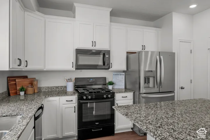 Kitchen featuring white cabinetry, speckled countertops, stainless steel refrigerator, black gas range, and built-in microwave