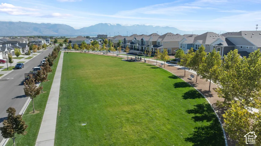 Expansive green space featuring a paved walking path, mature trees, and mountain backdrop