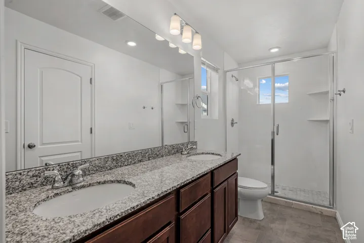 Dual vanity with stone-finish countertop, wood-finish cabinetry, and  dule undermount sinks, walk in shower, glass shower door