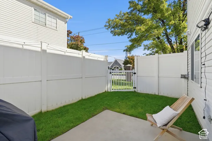 Private outdoor space featuring a manicured lawn, concrete patio, white privacy fencing, and a white picket gate