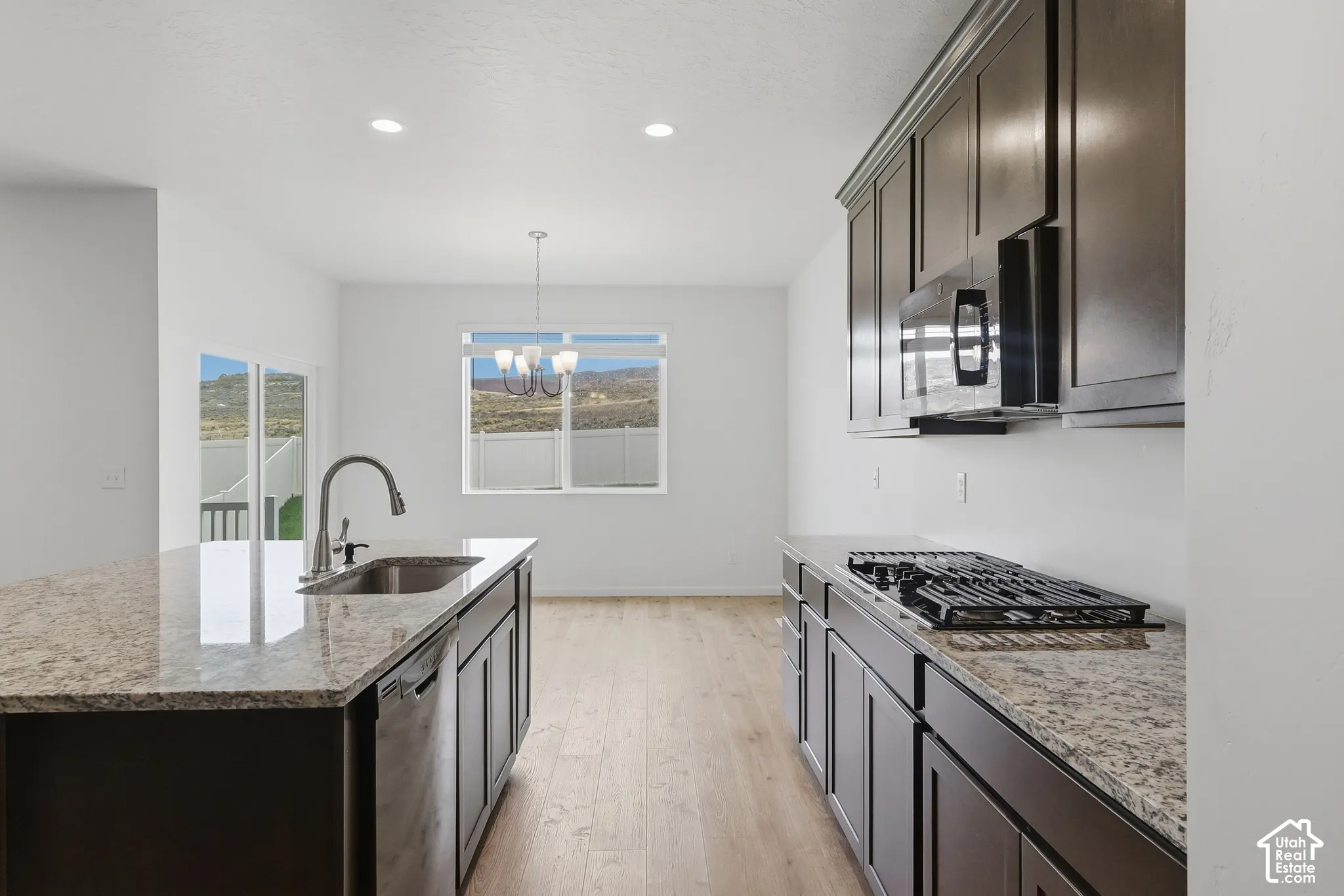 Kitchen featuring dark wood cabinetry, granite countertops, stainless steel sink with gooseneck faucet, built-in microwave, and gas cooktop