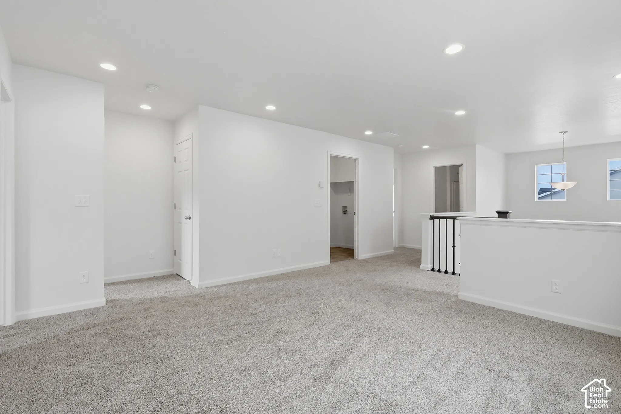 Spacious open area featuring recessed lighting, light-toned carpeting, and a stairway with black metal balusters