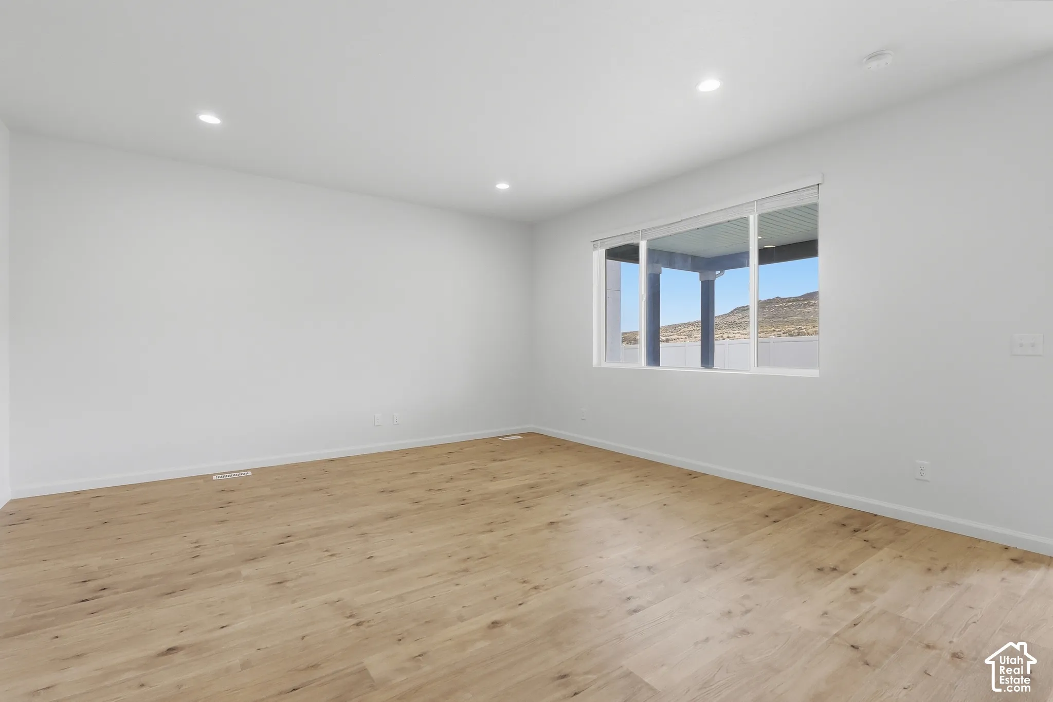 Light wood-finish flooring, recessed ceiling lighting, a large window, and white walls