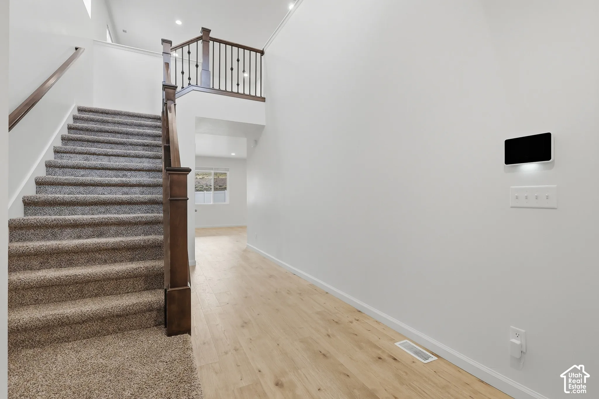 Carpeted staircase with dark wood newel posts and spindles, wood-finish flooring, white walls, and an upper landing with matching railing