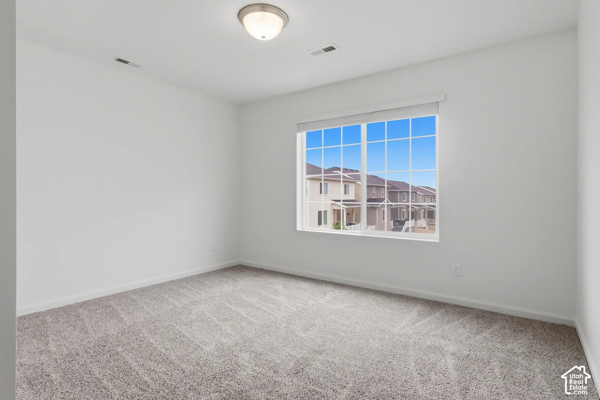 Neutral-toned carpeting, white walls, and a large window with white blinds
