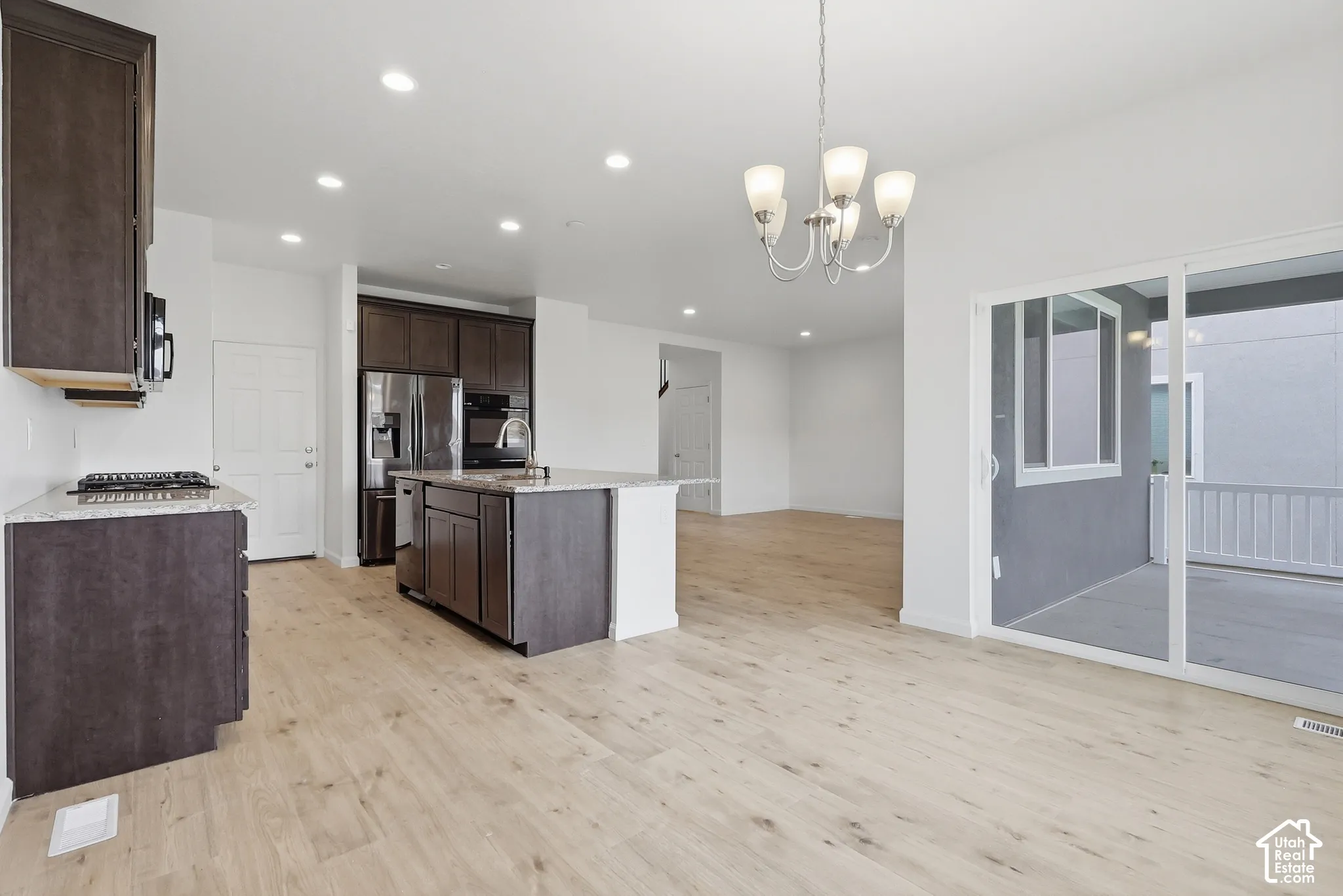 Open-concept kitchen with dark wood-finish cabinetry, a central island featuring a stainless steel sink, and light-toned wood-finish flooring
