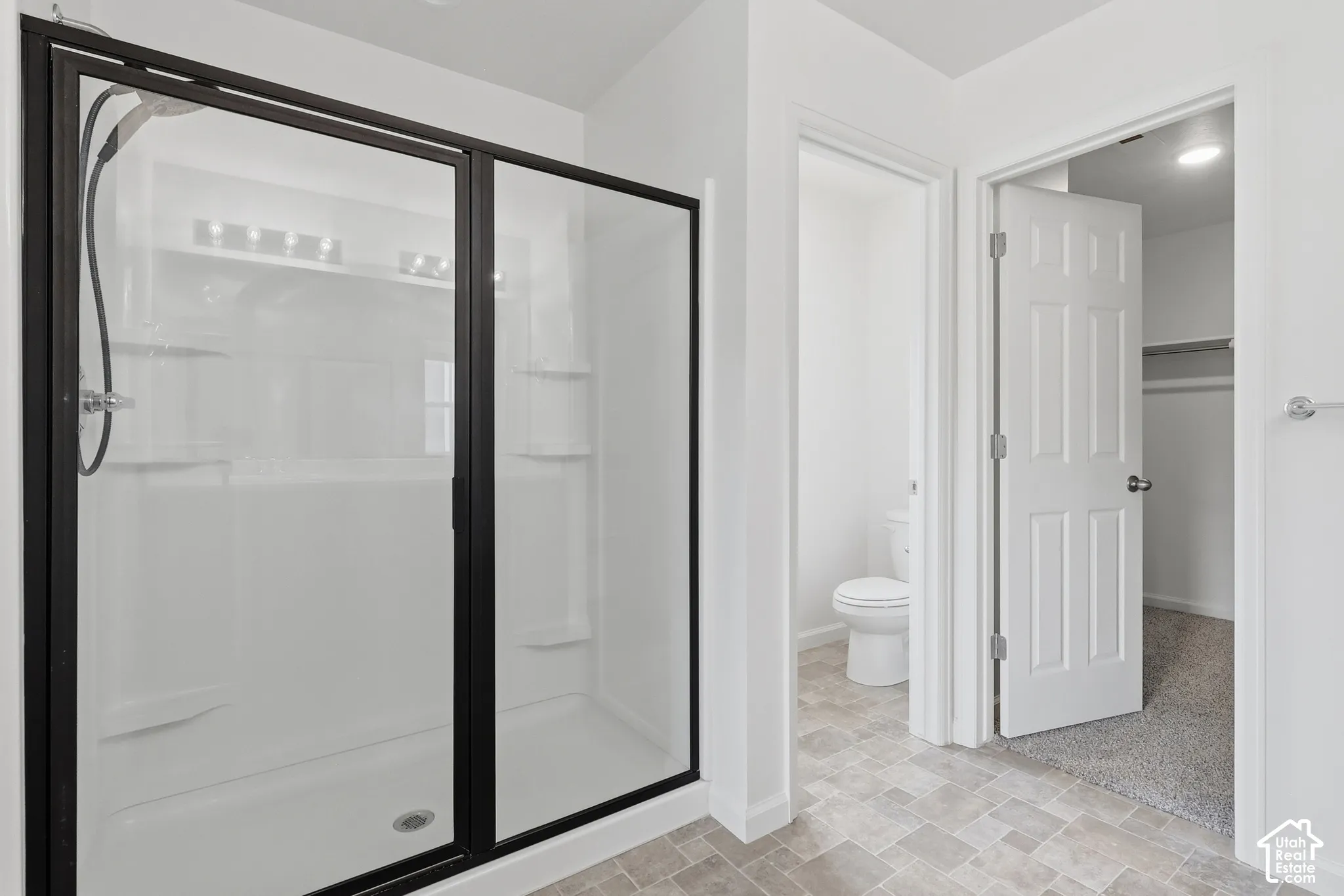 Shower with dark-framed sliding glass doors, built-in shelving, and white surround