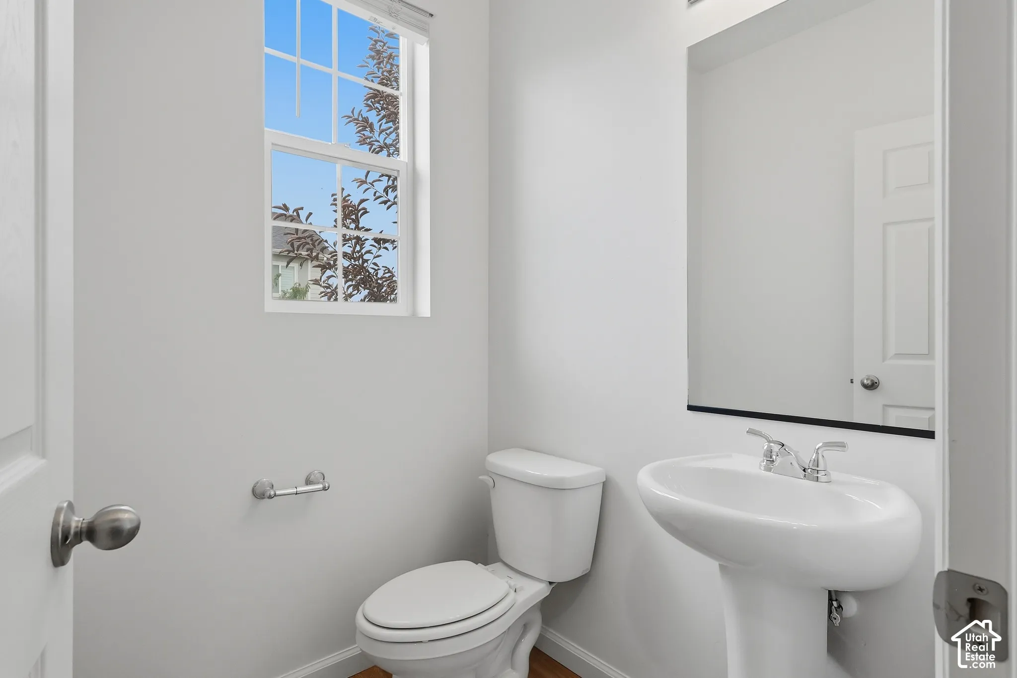 Pedestal sink with chrome fixtures, large wall-mounted mirror, and white paneled door
